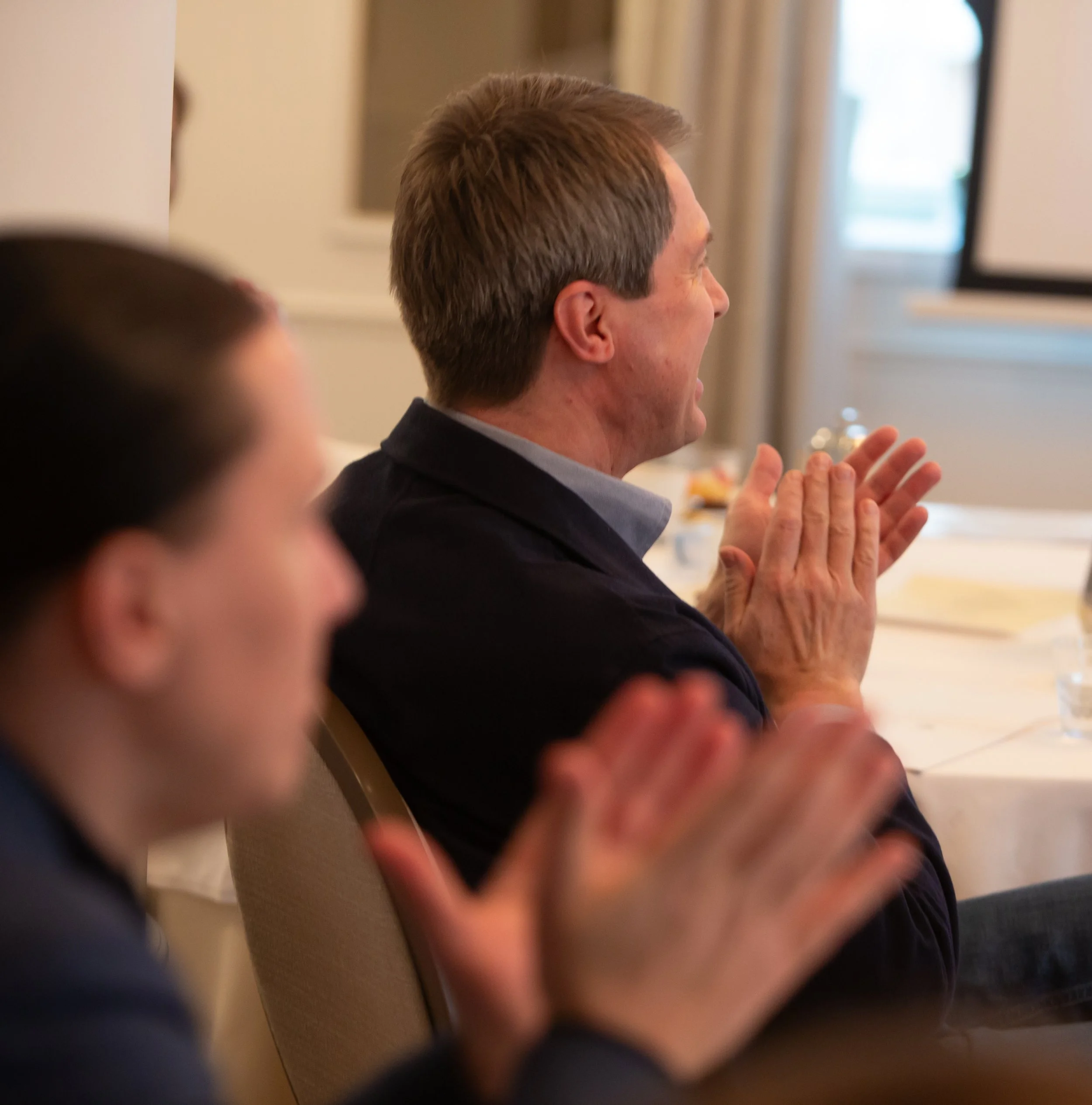 Kaksi miestä istuu konferenssissa ja taputtaa.