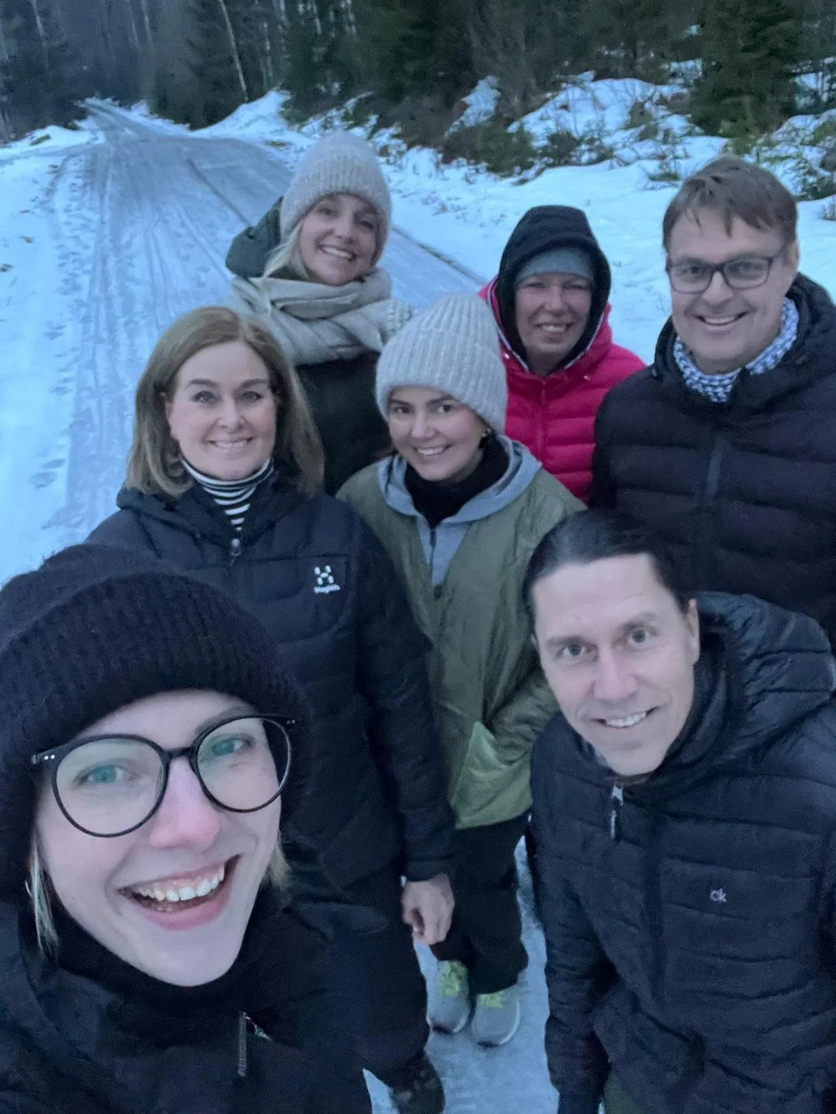 Seitsemän ihmistä ottavat ryhmäkuvaa lumisella tiellä metsässä.