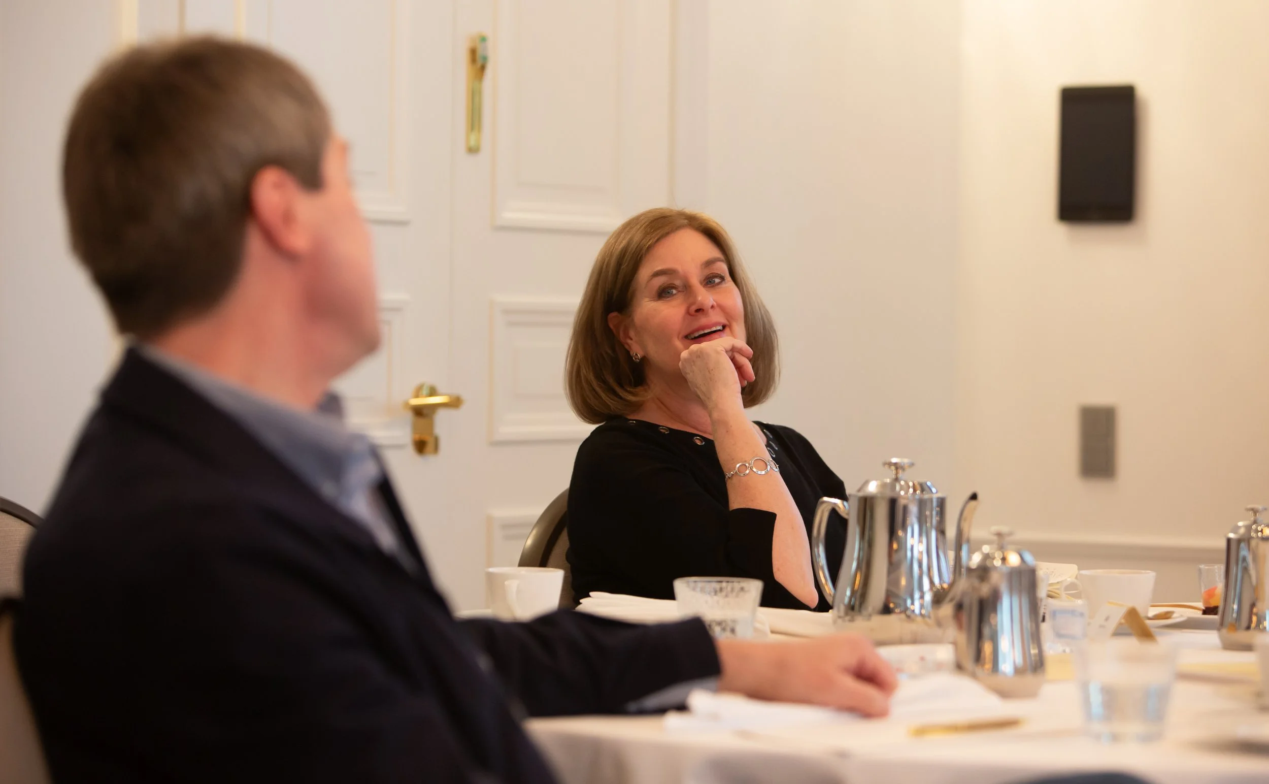 Nainen ja mies istuvat pöydän ääressä keskustelussa, nainen hymyilee.