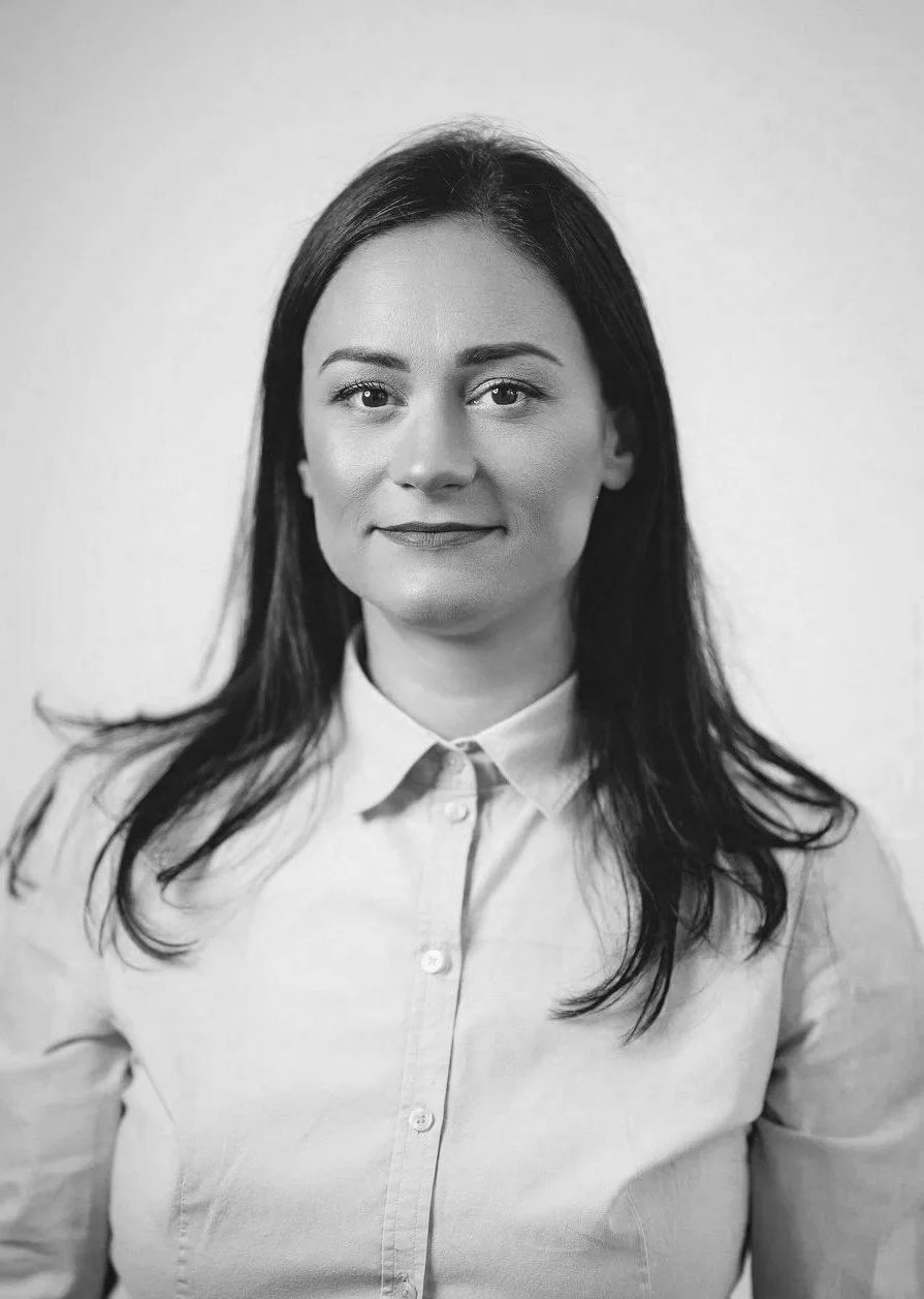 Portræt af en kvinde i lyseblå skjorte og mørk jakke på en neutral baggrund.