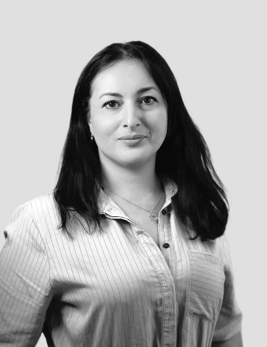 Portræt af en kvinde i lyseblå skjorte og mørk jakke på en neutral baggrund.