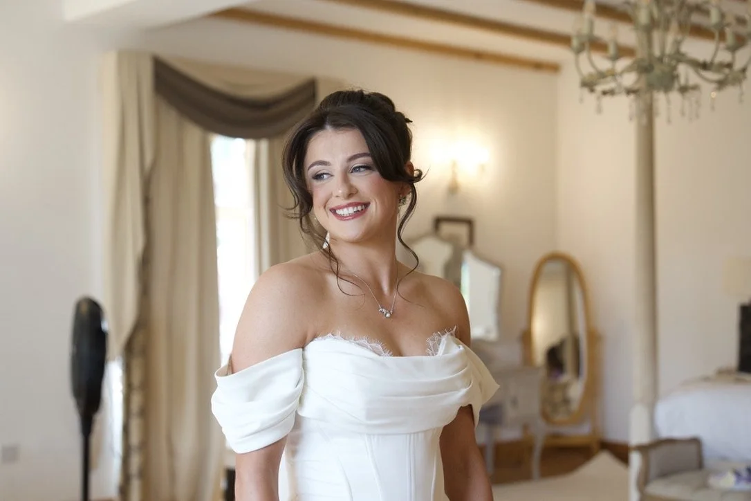 Bride in a white wedding dress smiling in a well-lit room with elegant decor.