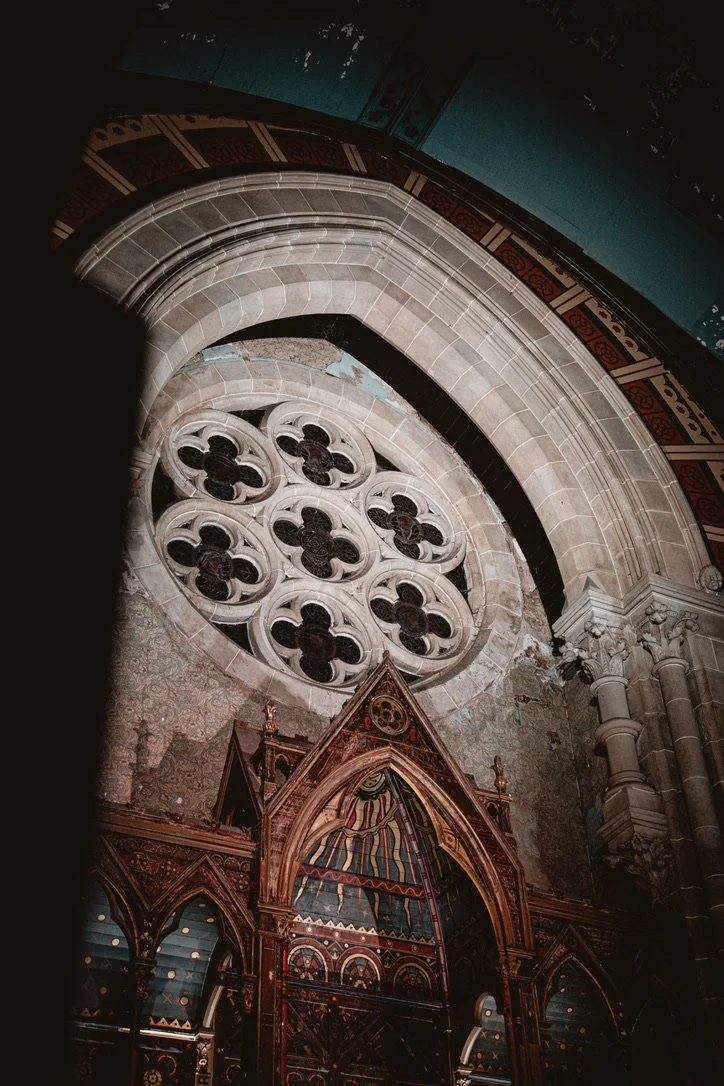 Interior view of a Gothic cathedral showcasing a large rose window with stained glass and surrounding stone arches, columns, and intricate architectural details.