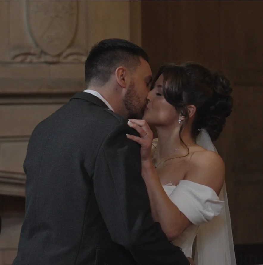 A man and woman in wedding attire sharing a kiss, with the woman touching the man's shoulder.