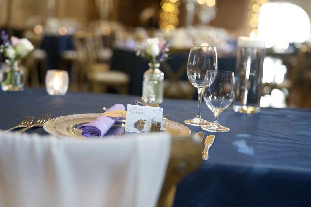 Elegant dining table setup with purple napkin, glassware, and a unique place card with a fox illustration, set for a formal event.