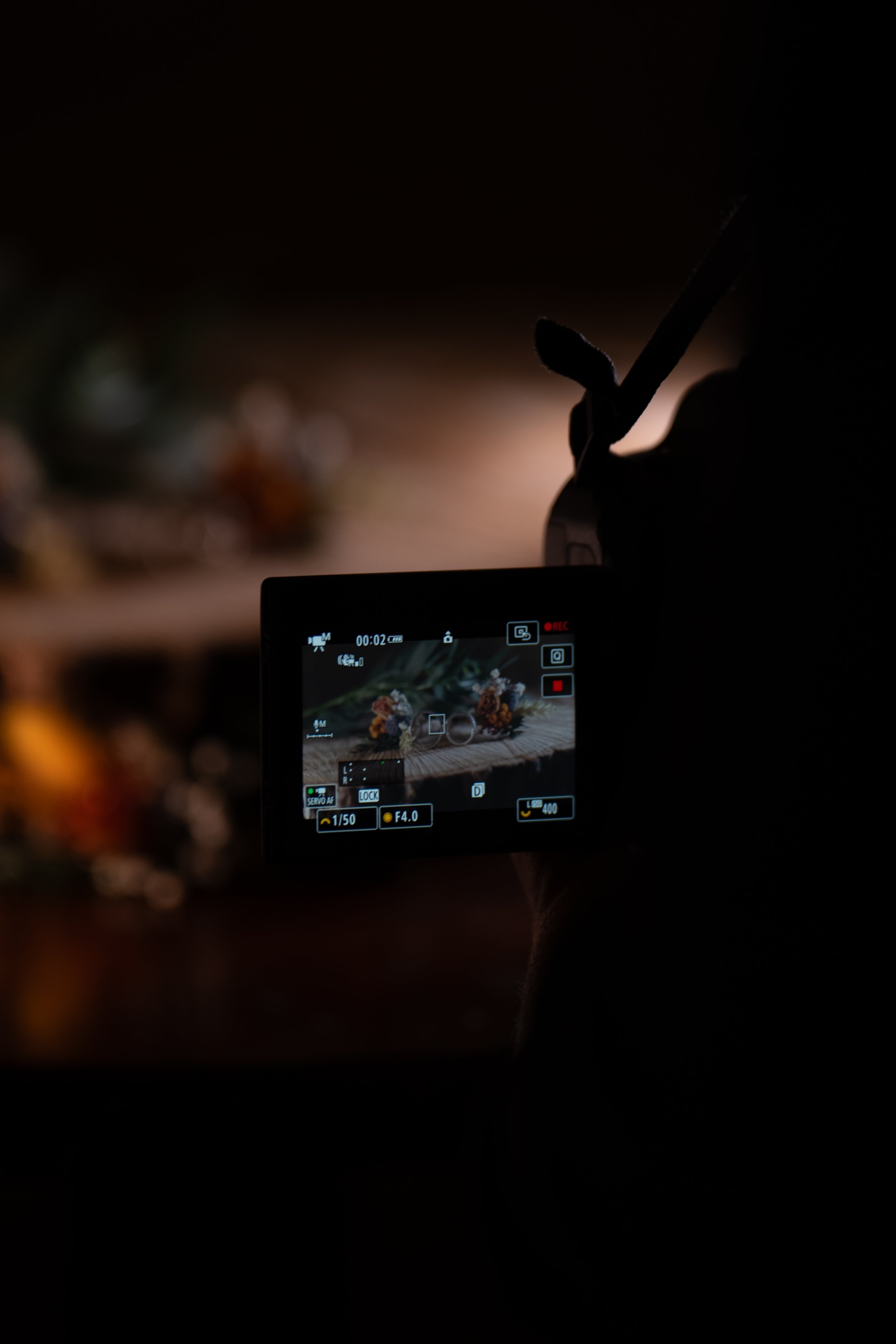 A person filming flowers with a camera in a dark setting.
