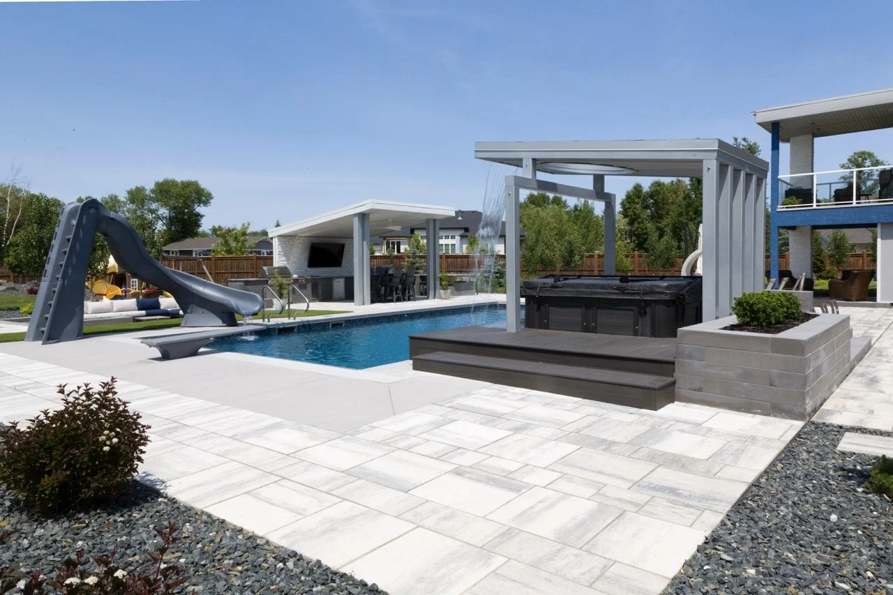Outdoor pool area with a waterslide, pergola, hot tub, and a covered patio with seating, surrounded by modern landscaping and stone tiles.