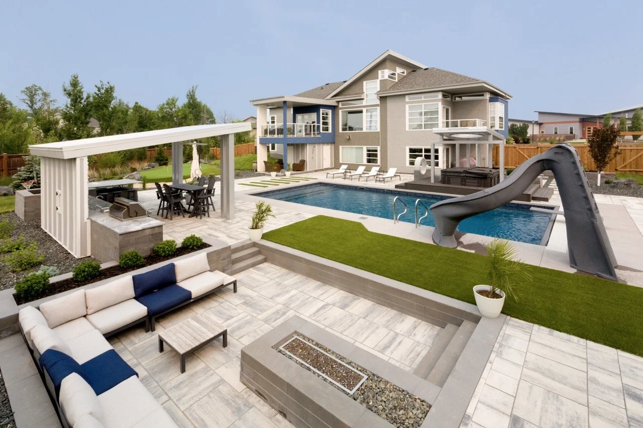 Modern backyard with pool, slide, patio seating, outdoor kitchen, and pergola.