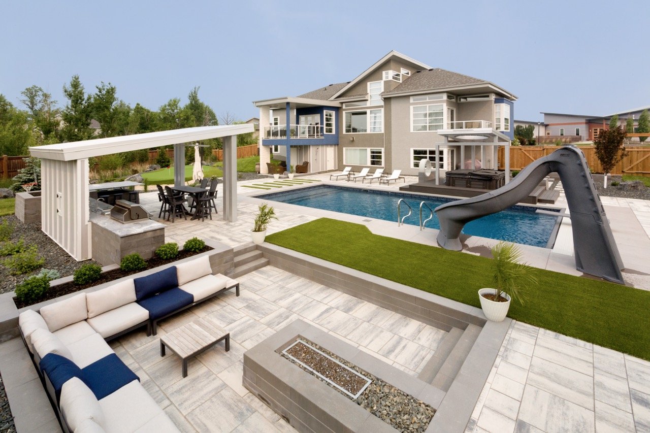 Luxury backyard with swimming pool, slide, patio, outdoor furniture, covered dining area, and modern house in background.