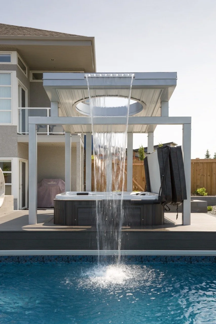 Modern outdoor patio setup with a hot tub under a pergola, featuring a waterfall cascading into a swimming pool.