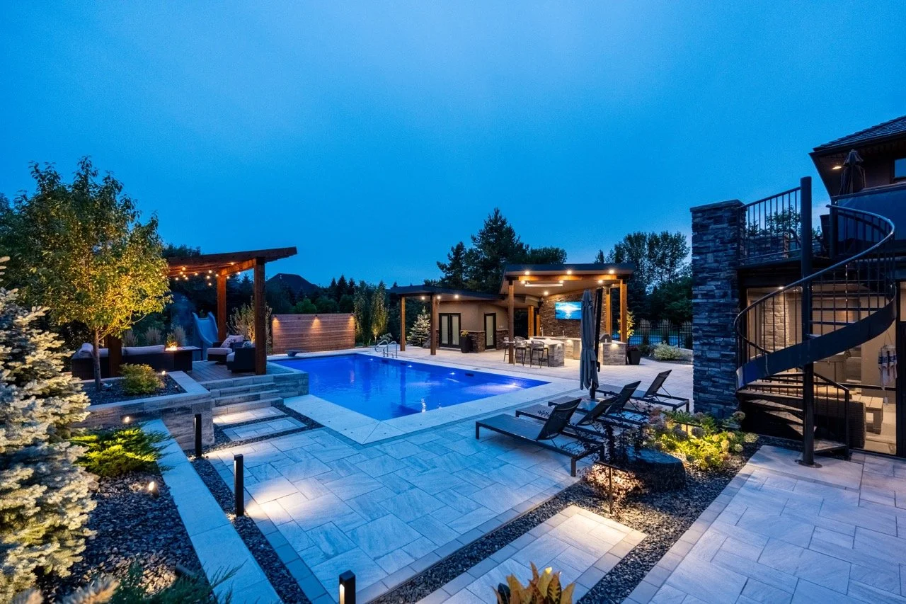 Luxury outdoor patio with illuminated swimming pool, seating area under pergola, and spiral staircase at dusk.