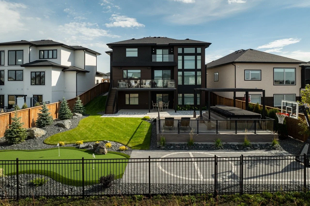 Backyard with mini golf, basketball court, patio, and modern black and white houses on a sunny day.