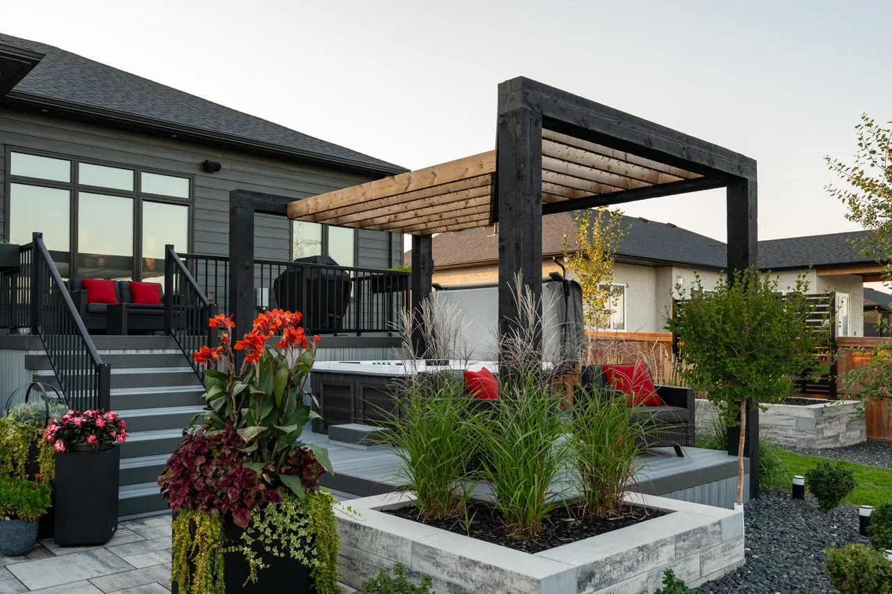 Modern backyard with a deck, steps, and outdoor furniture, including a hot tub, plants, and a pergola structure.