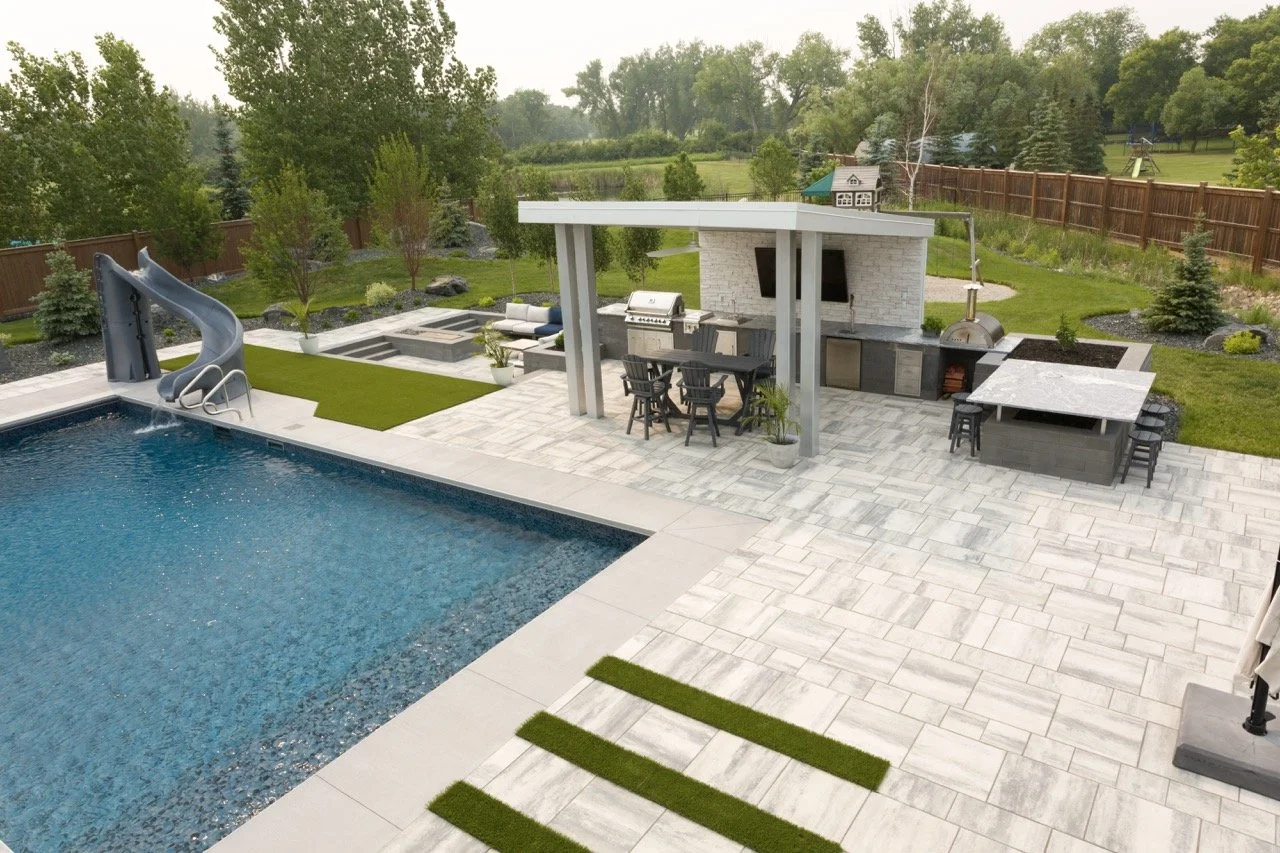 Modern backyard with swimming pool, water slide, outdoor kitchen, dining area, and a spacious patio.