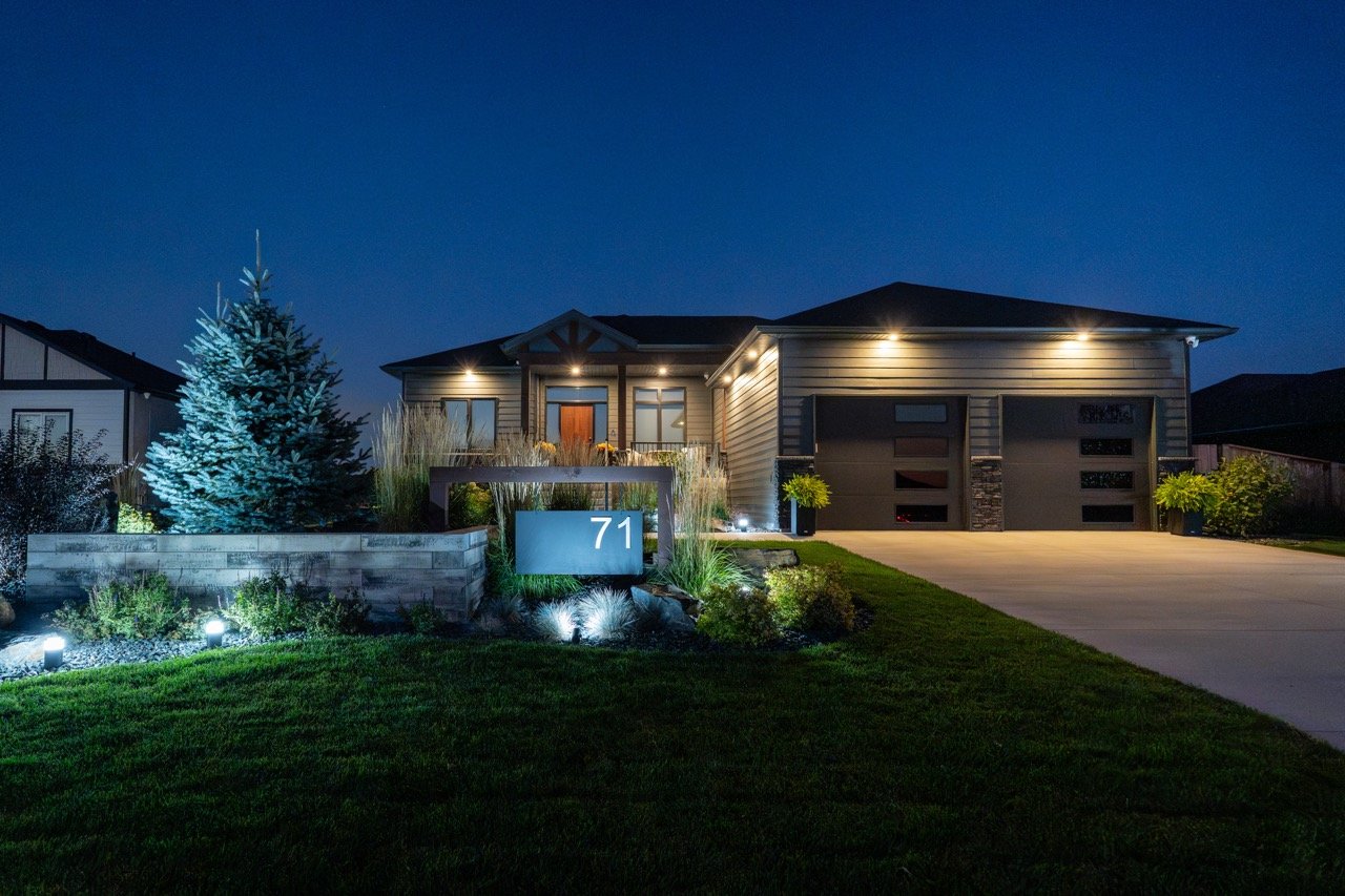 Night view of a modern house with exterior lighting, a driveway, and landscaped yard with a lit sign displaying the number 71.