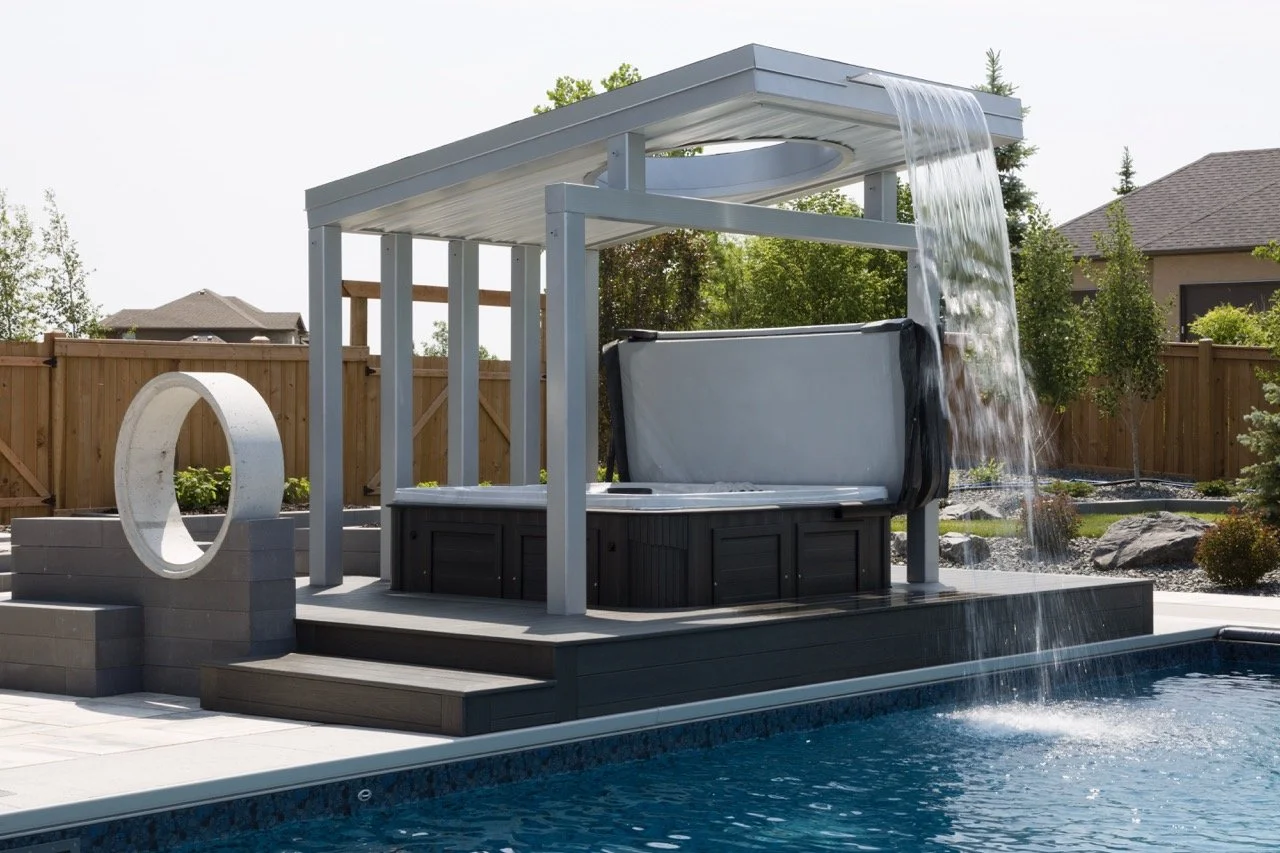 Backyard patio with hot tub under modern pergola, waterfall feature into swimming pool, and circular concrete sculpture.