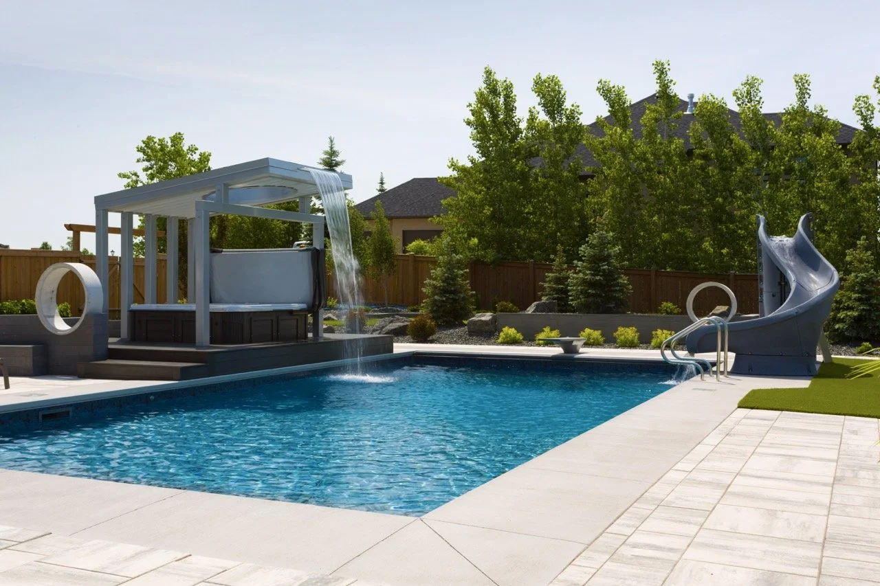 Backyard pool with water slide, hot tub with canopy, water feature, and surrounding greenery.