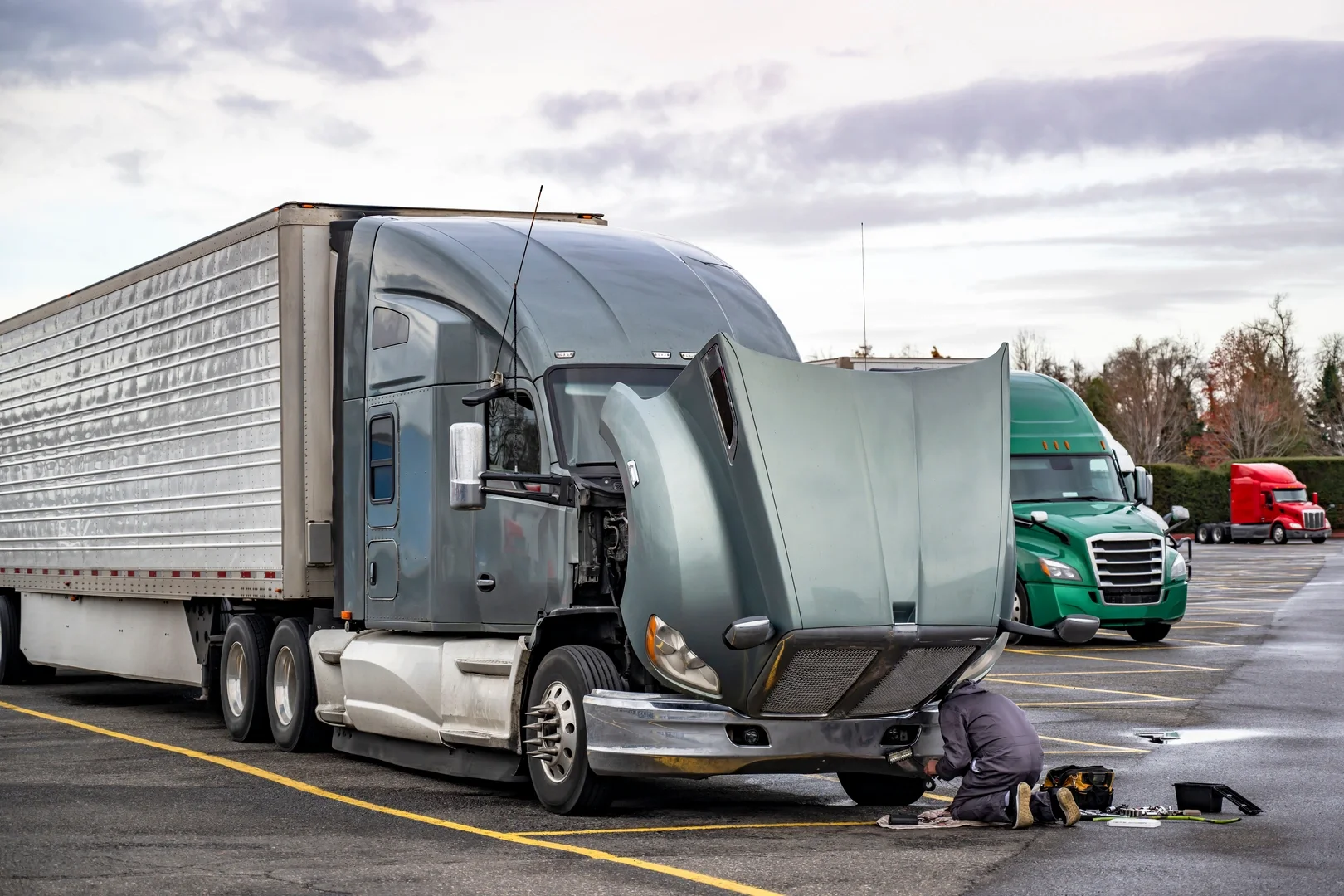 Mechanic repairing a semi truck with hood open in a parking lot
