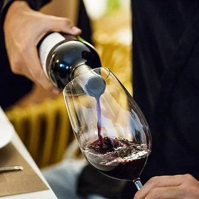 Persona versa vino rosso in un bicchiere.