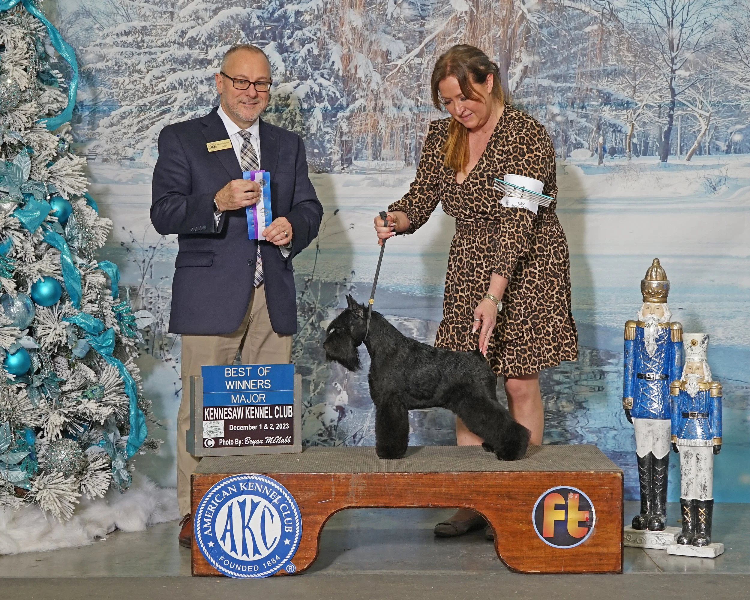 Dog show winner with handler and official at Kennesaw Kennel Club event, winter-themed background.