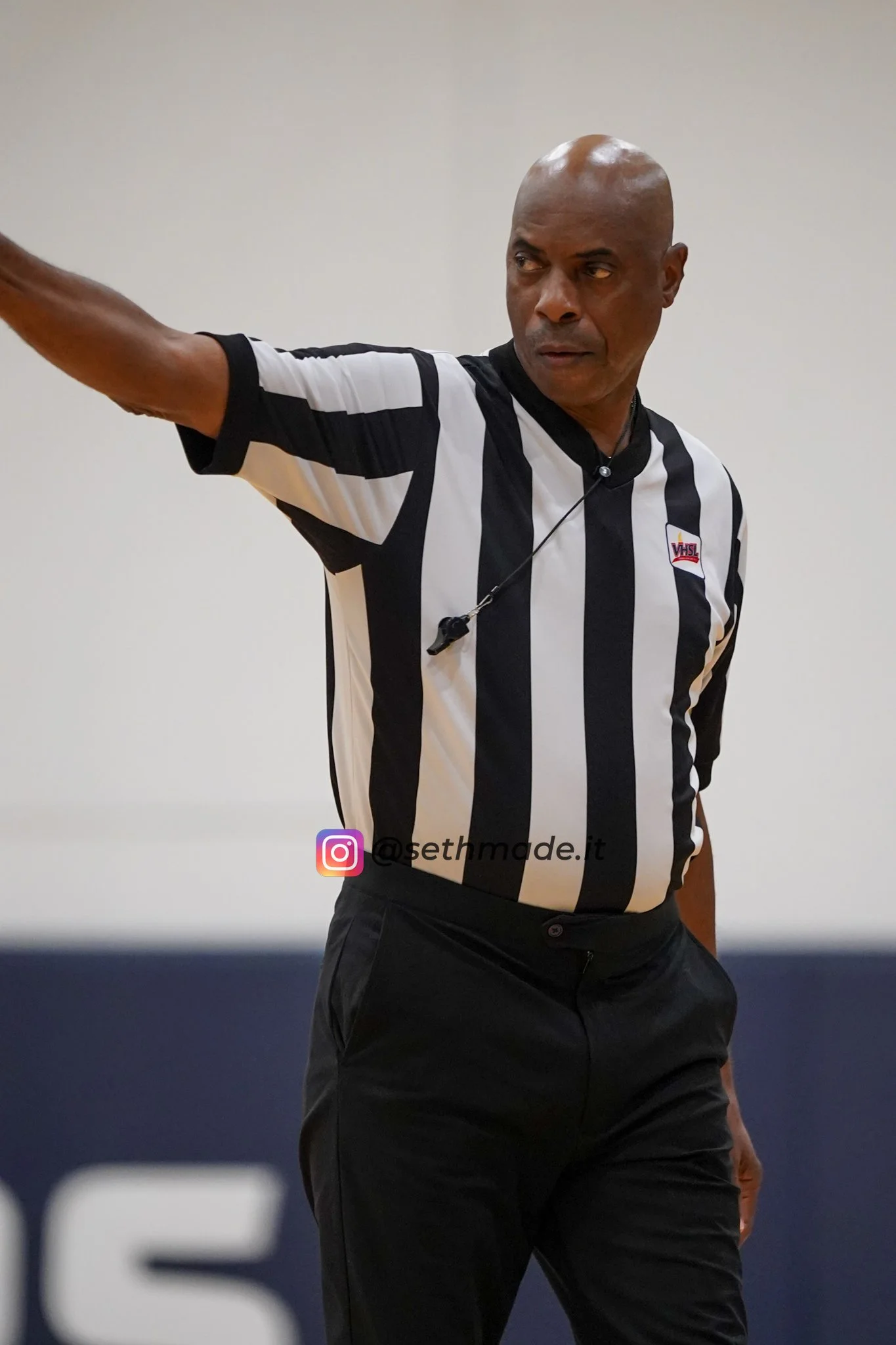 A male basketball referee in a black and white striped shirt, pointing with his right arm, during a game.