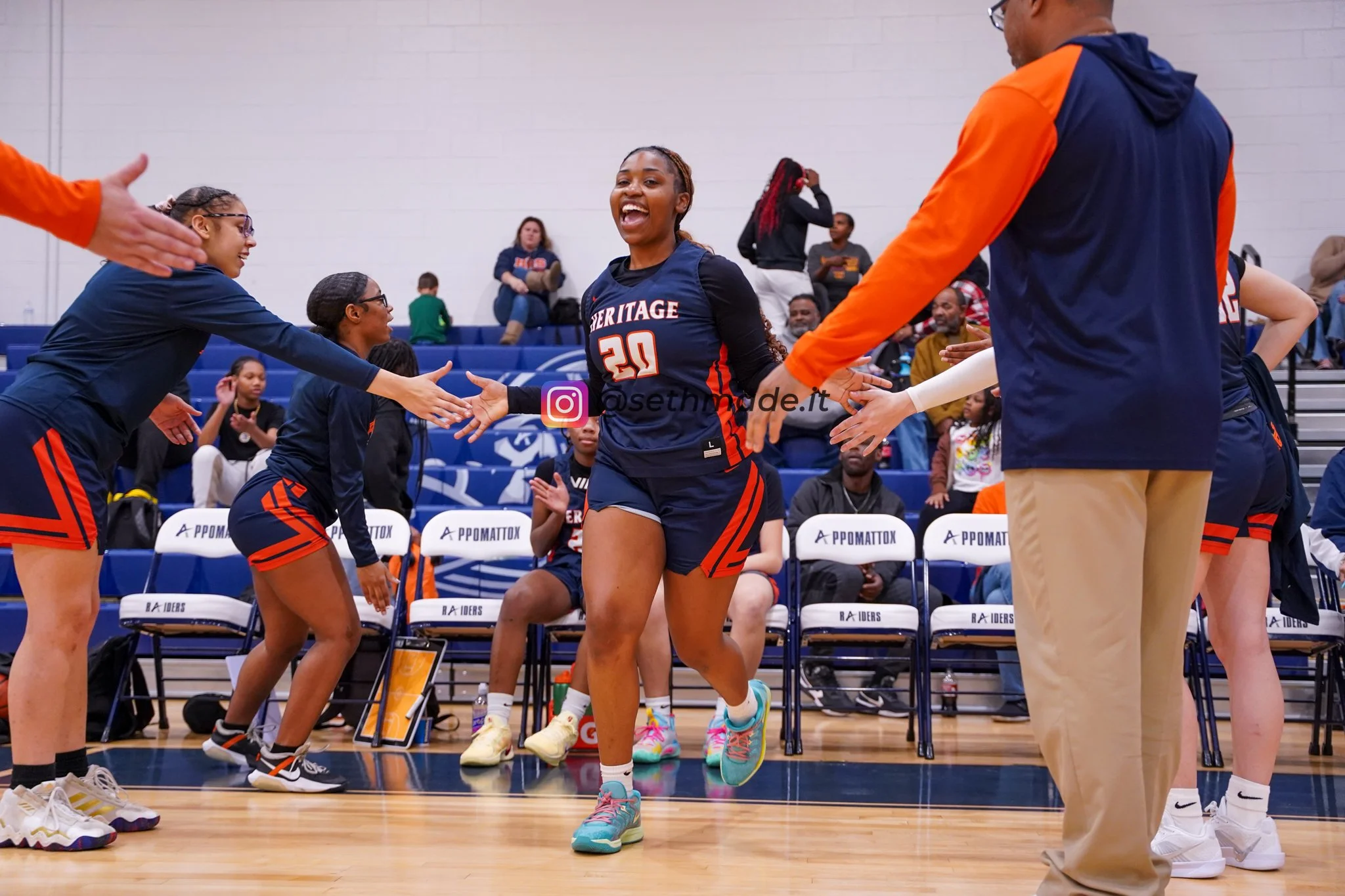 A female basketball player wearing jersey number 20 is smiling and running through a handshake line with teammates and coaches during a game. She appears happy and energetic.