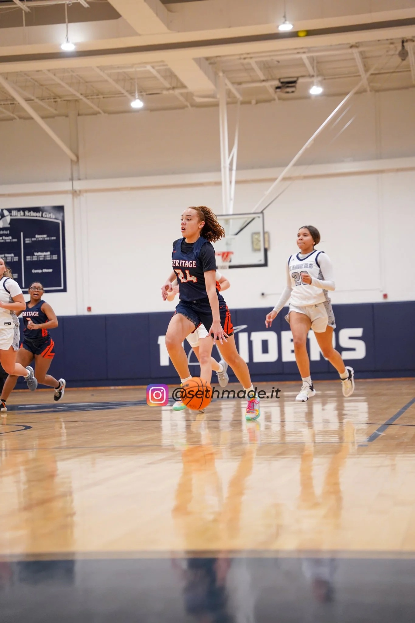 Young female basketball players running on the court during a game, with one player dribbling the ball.