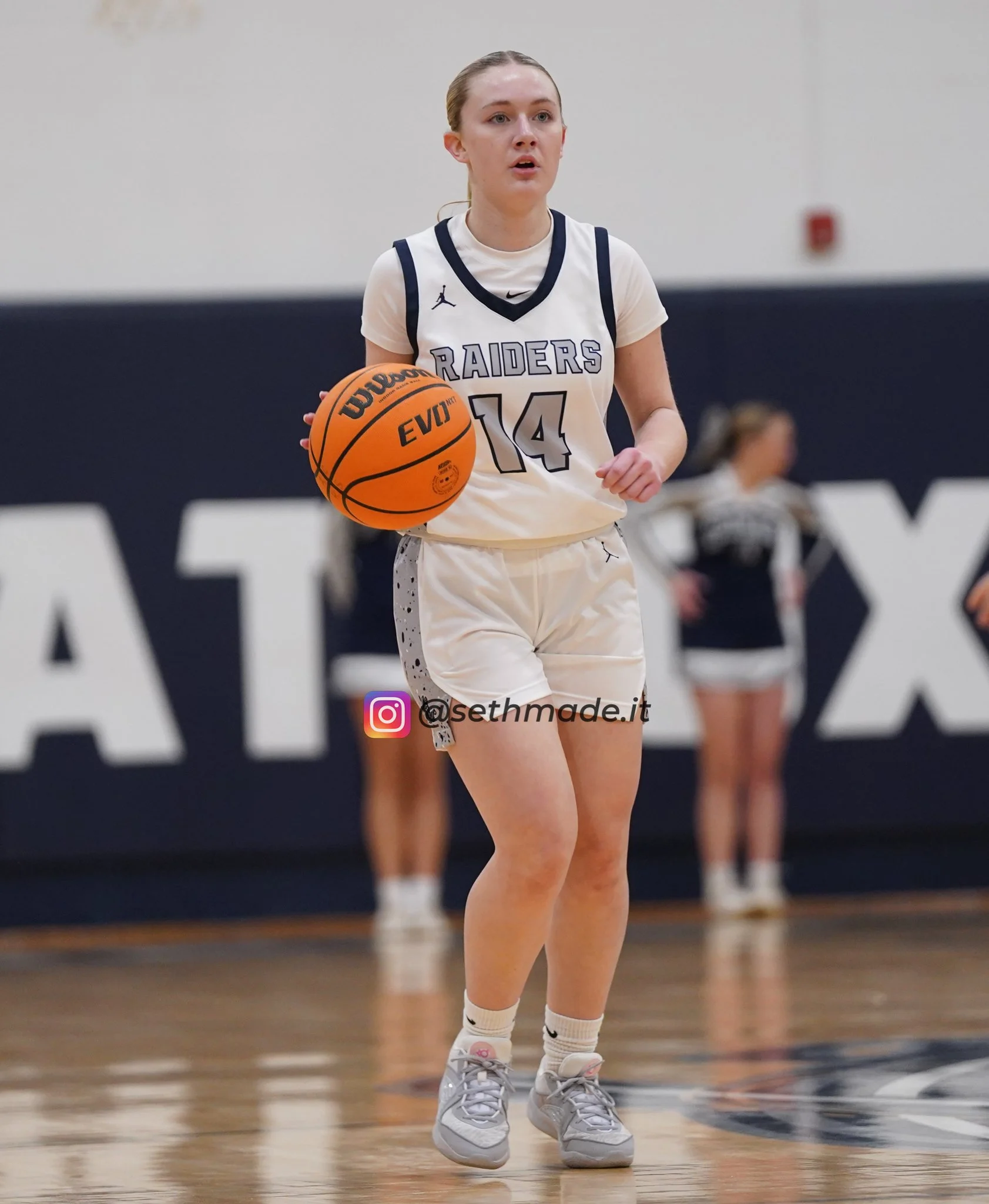 A female basketball player in uniform dribbling a basketball on indoor court with a focused expression.