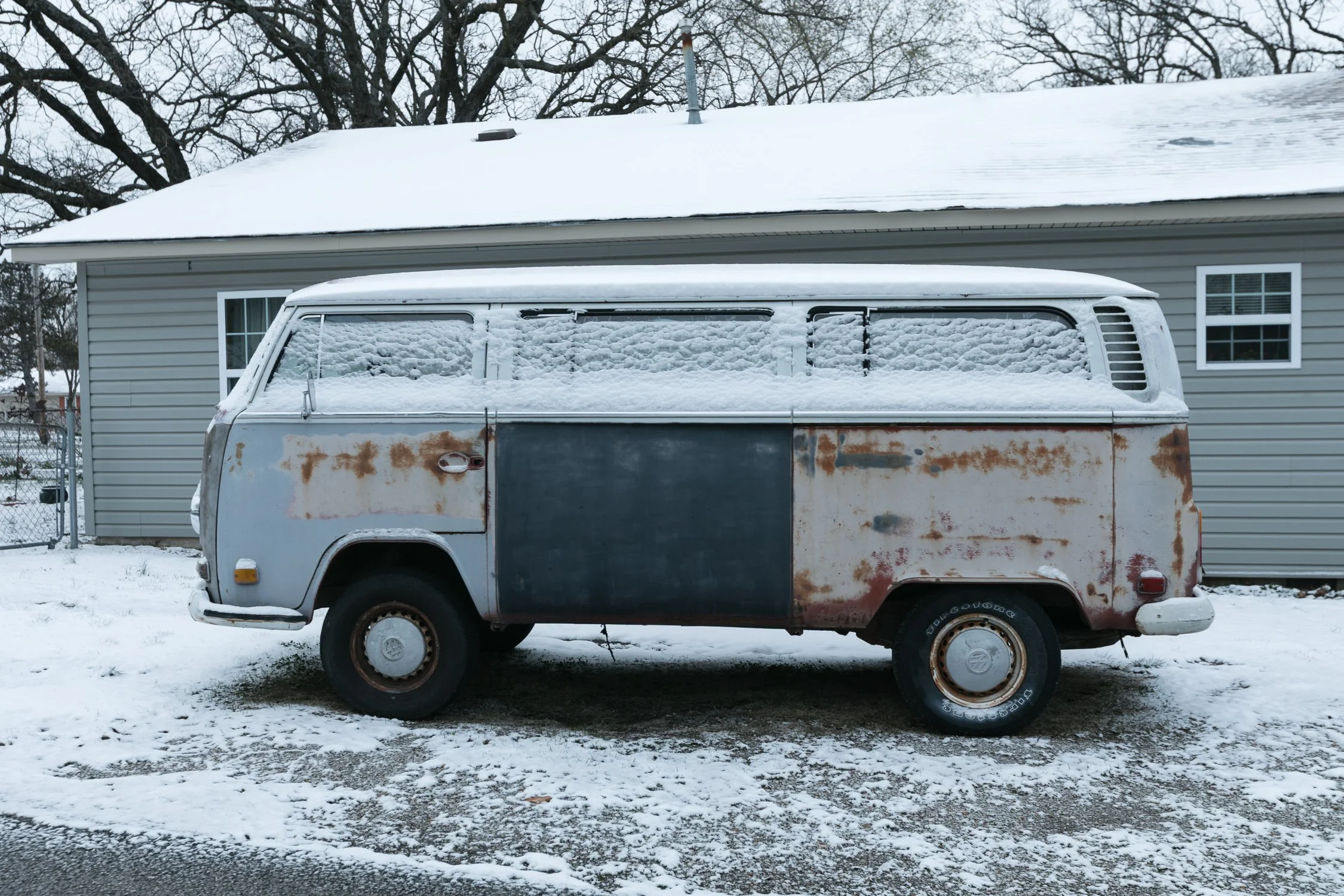 Combi Volkswagen oxidada sobre la nieve frente a una casa