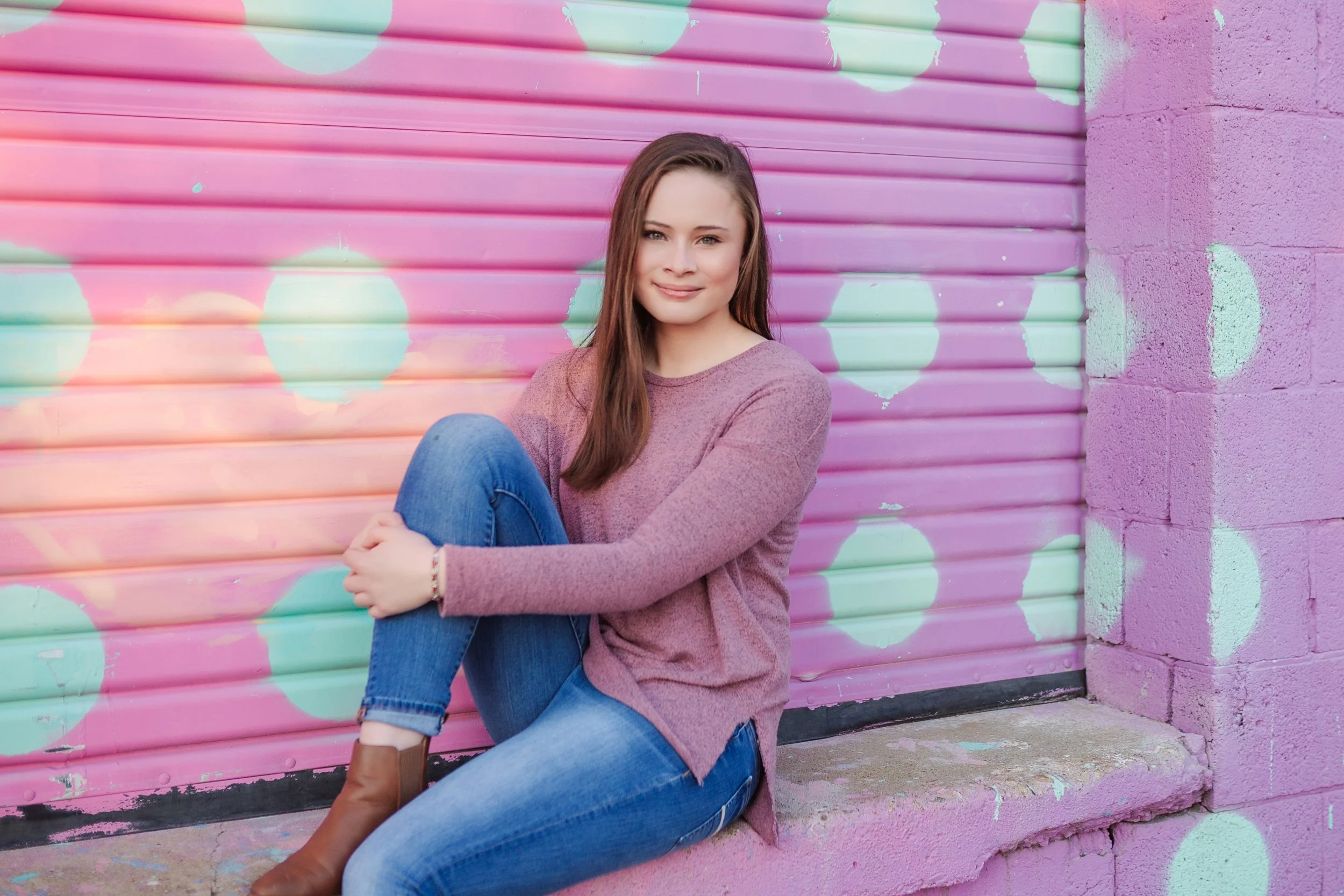 smiling high school senior girl in front of pink wall