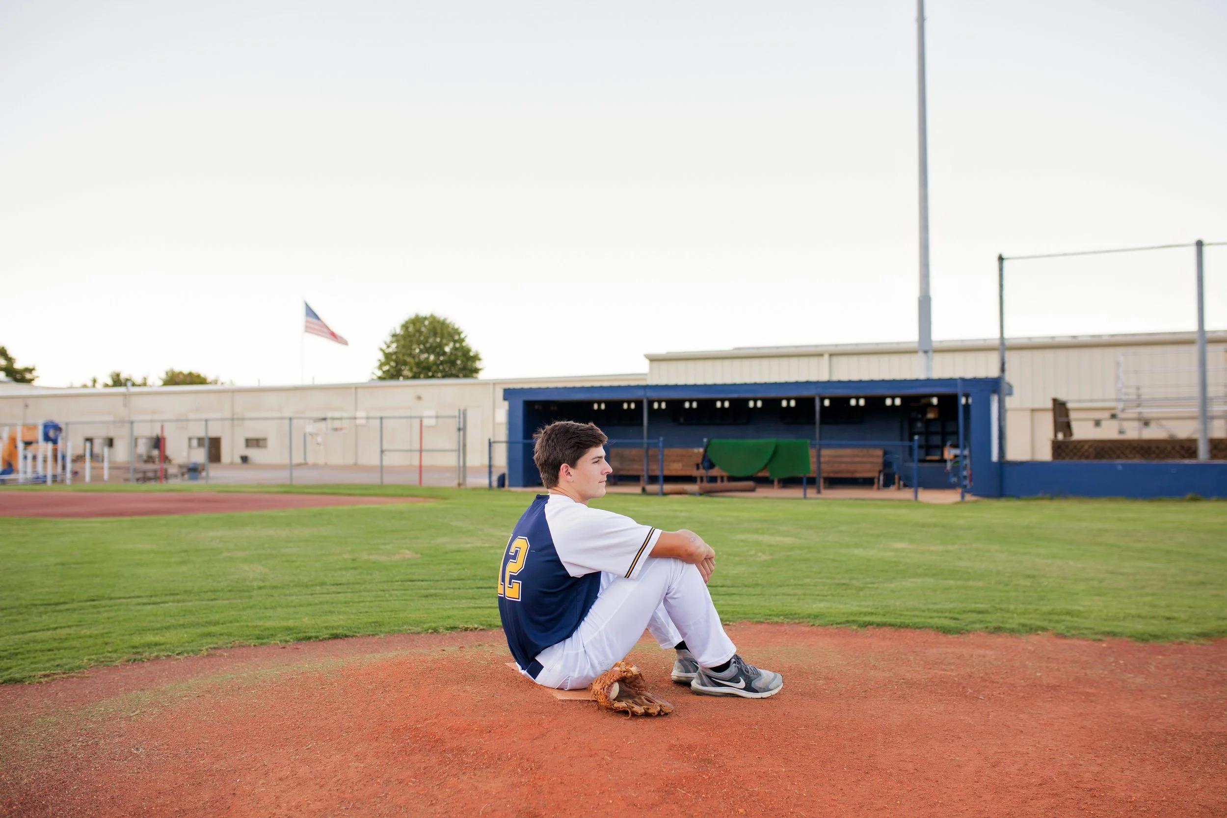a high school senior sitting on the field in his baseball uniform