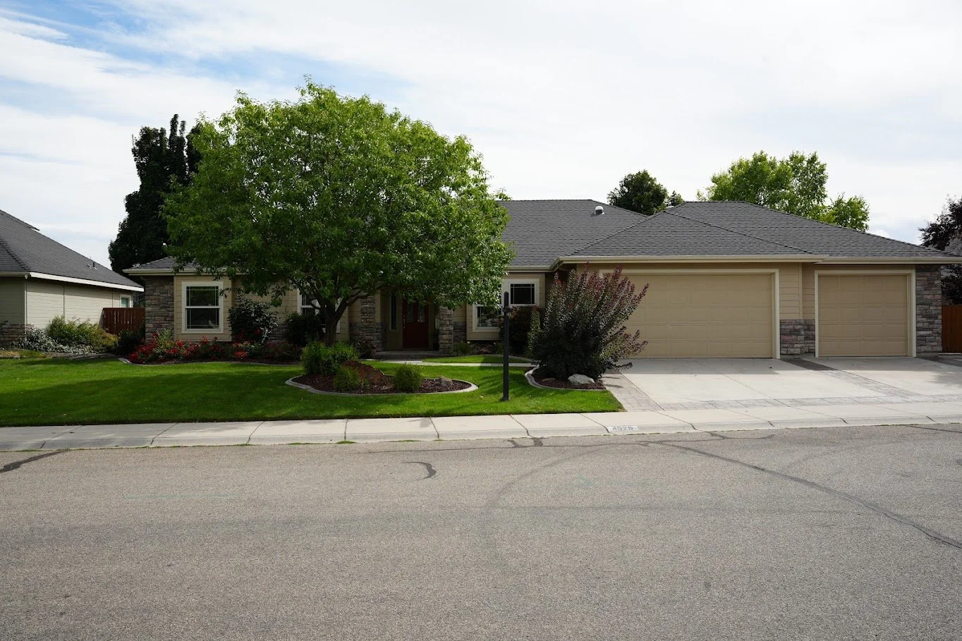 A suburban house with a well-maintained lawn, a large tree in front, and a two-car garage with beige doors.
