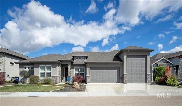 Modern gray house with attached garage, landscaped yard, neighborhood street, blue sky with clouds.