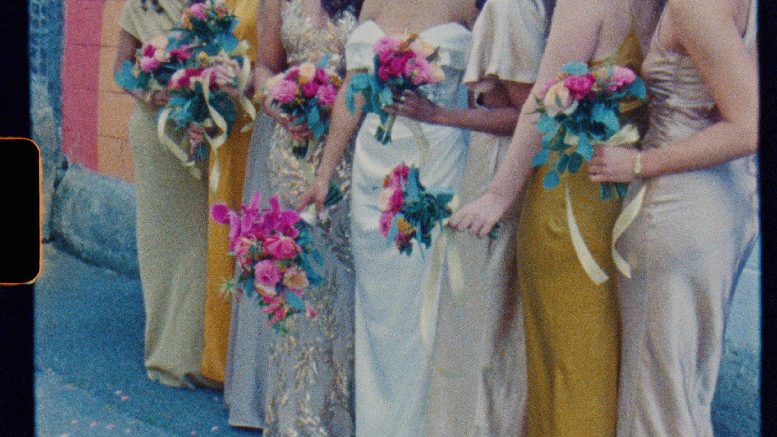 Five women standing in a line holding colorful flower bouquets, dressed in elegant dresses, at an outdoor event.