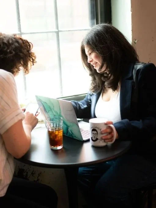 Carolyn LEasure, in a white tank and blue jacket, helping a client with website project prep
