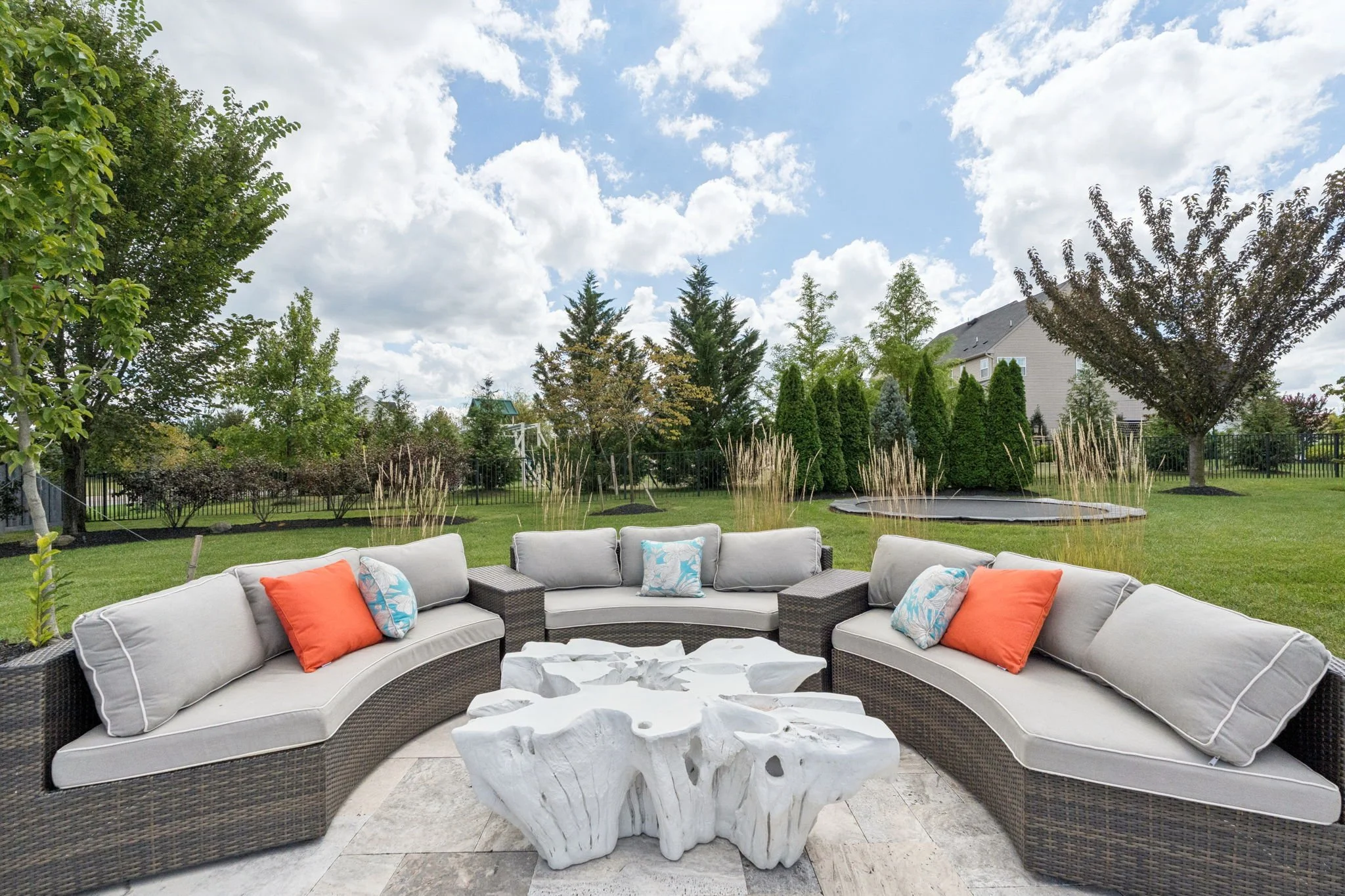 Curved outdoor sectional and stump-style coffee table on the travertine patio with evergreens behind