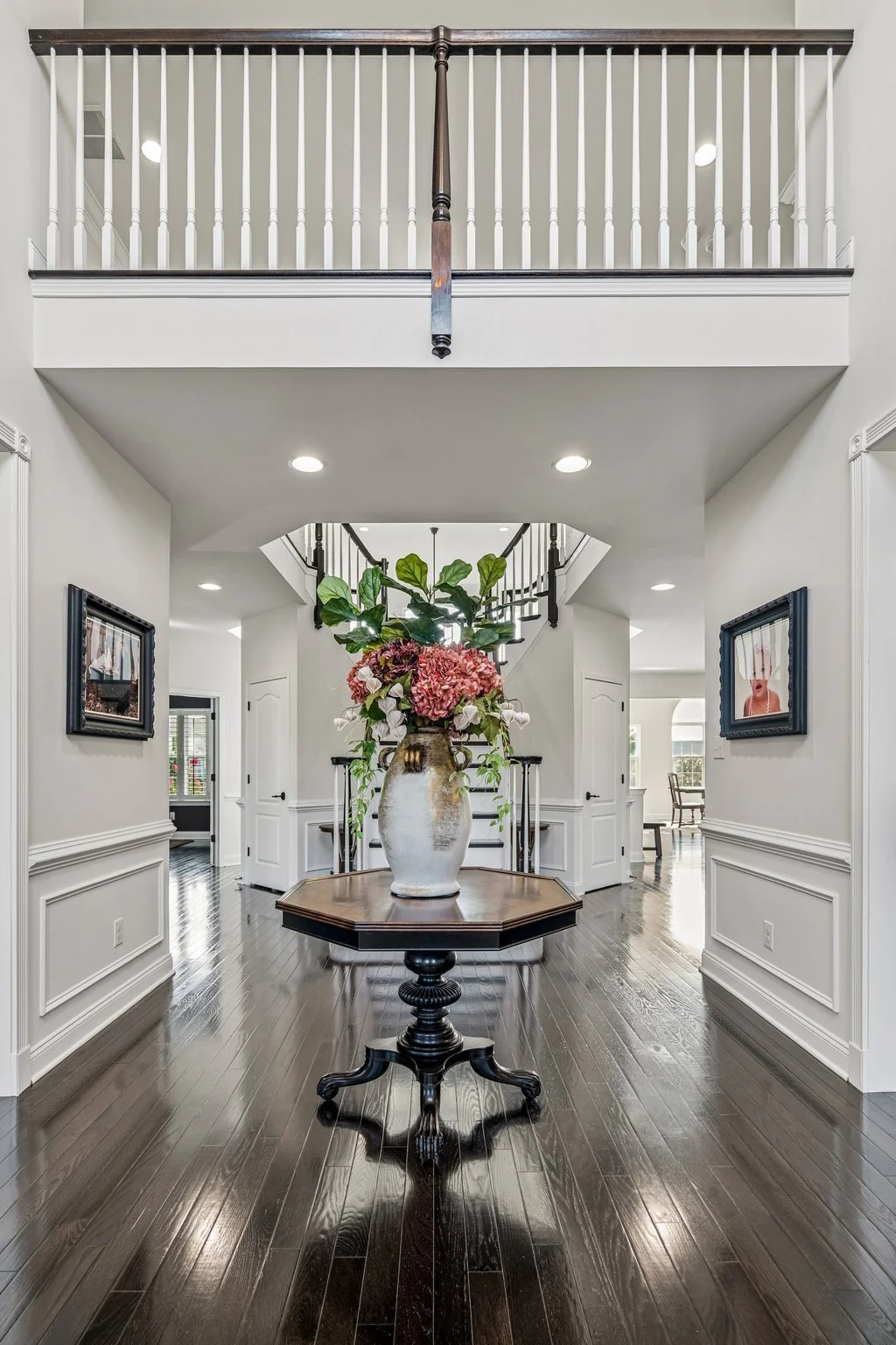 Two-story foyer with dark hardwood floors, wainscoting, an octagonal entry table, and an upstairs balcony