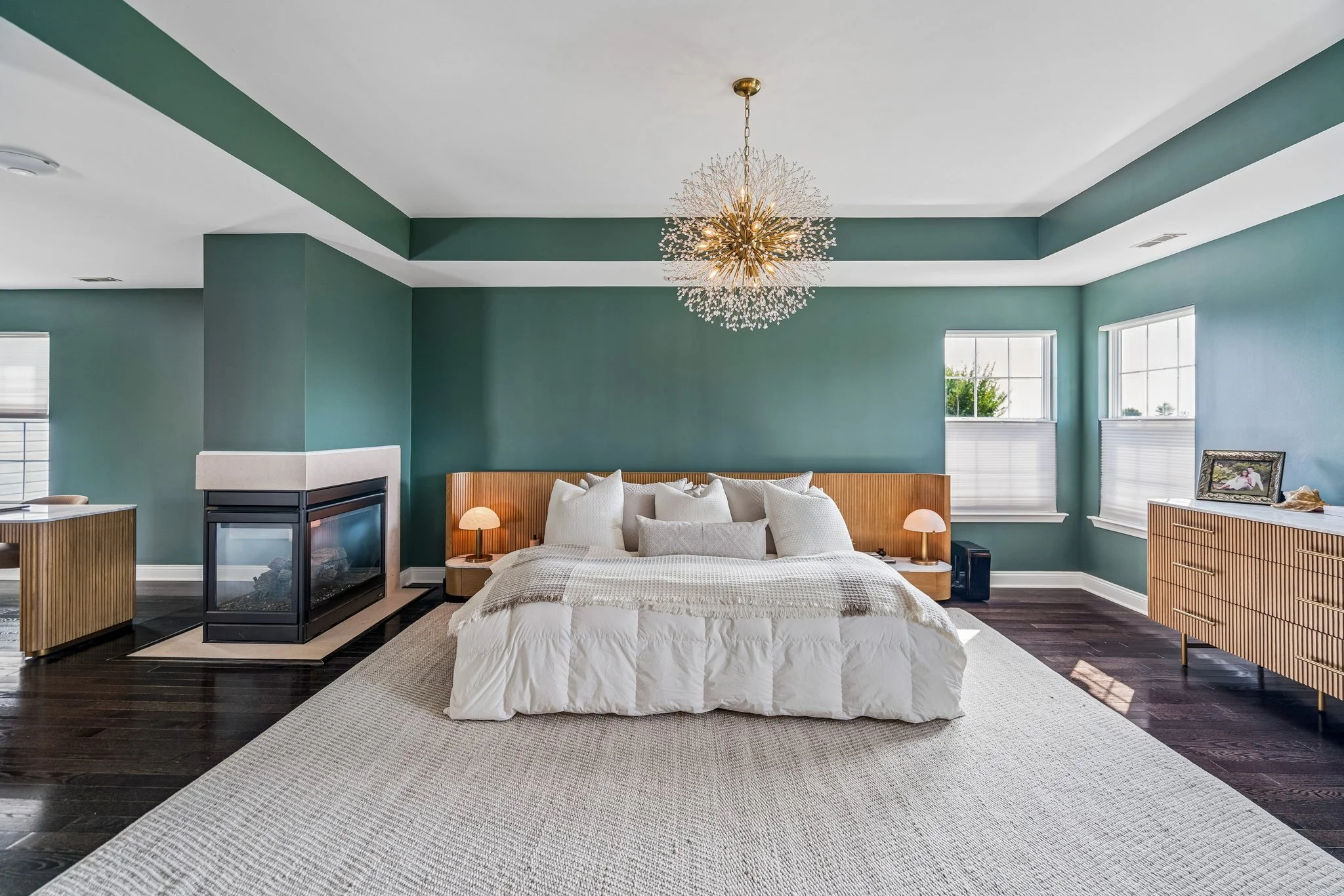 Primary bedroom with teal accent walls, a tray ceiling, sputnik chandelier, and a glass-front fireplace