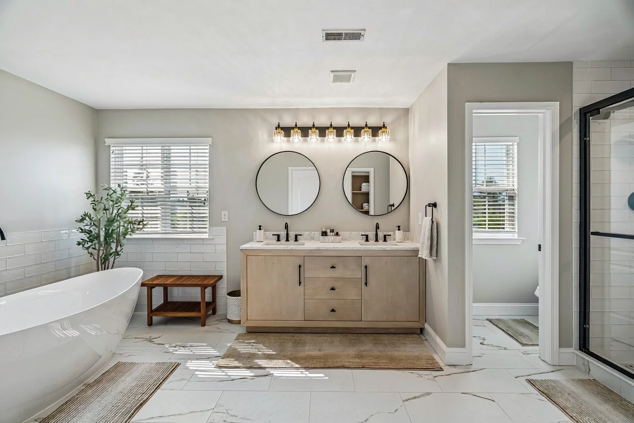 Primary bathroom with a freestanding soaking tub, double vanity with round mirrors, and a glass shower