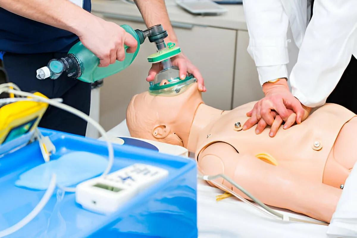 Medical professionals performing CPR on a medical training mannequin in a clinical setting.