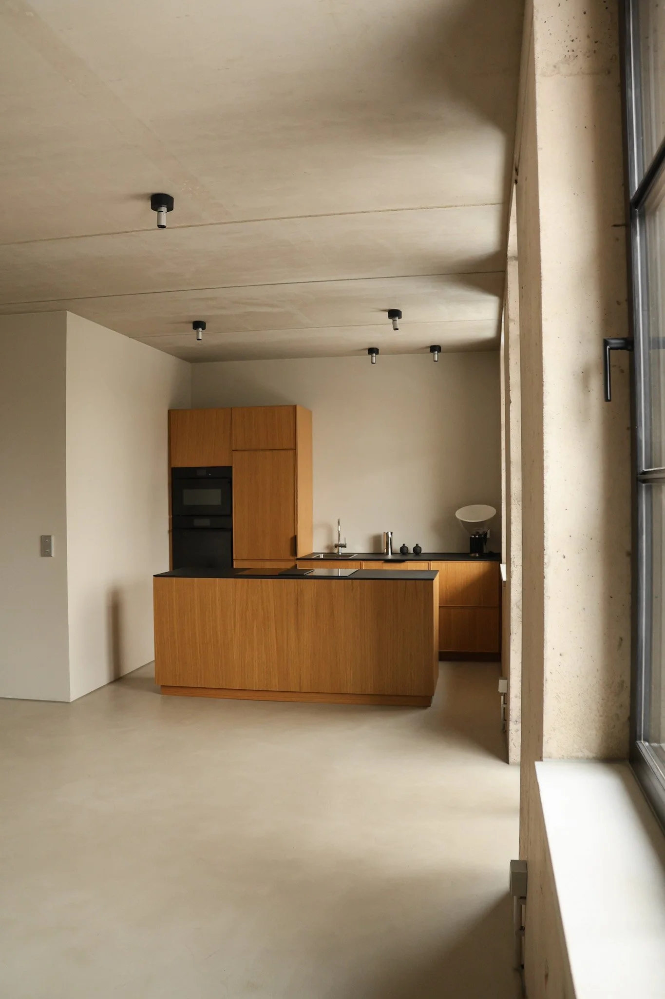 Moderne Küche mit Holzfronten, schwarzer Arbeitsfläche, großen Fenster, minimalistische Dekorationen und unbelebtem Licht.