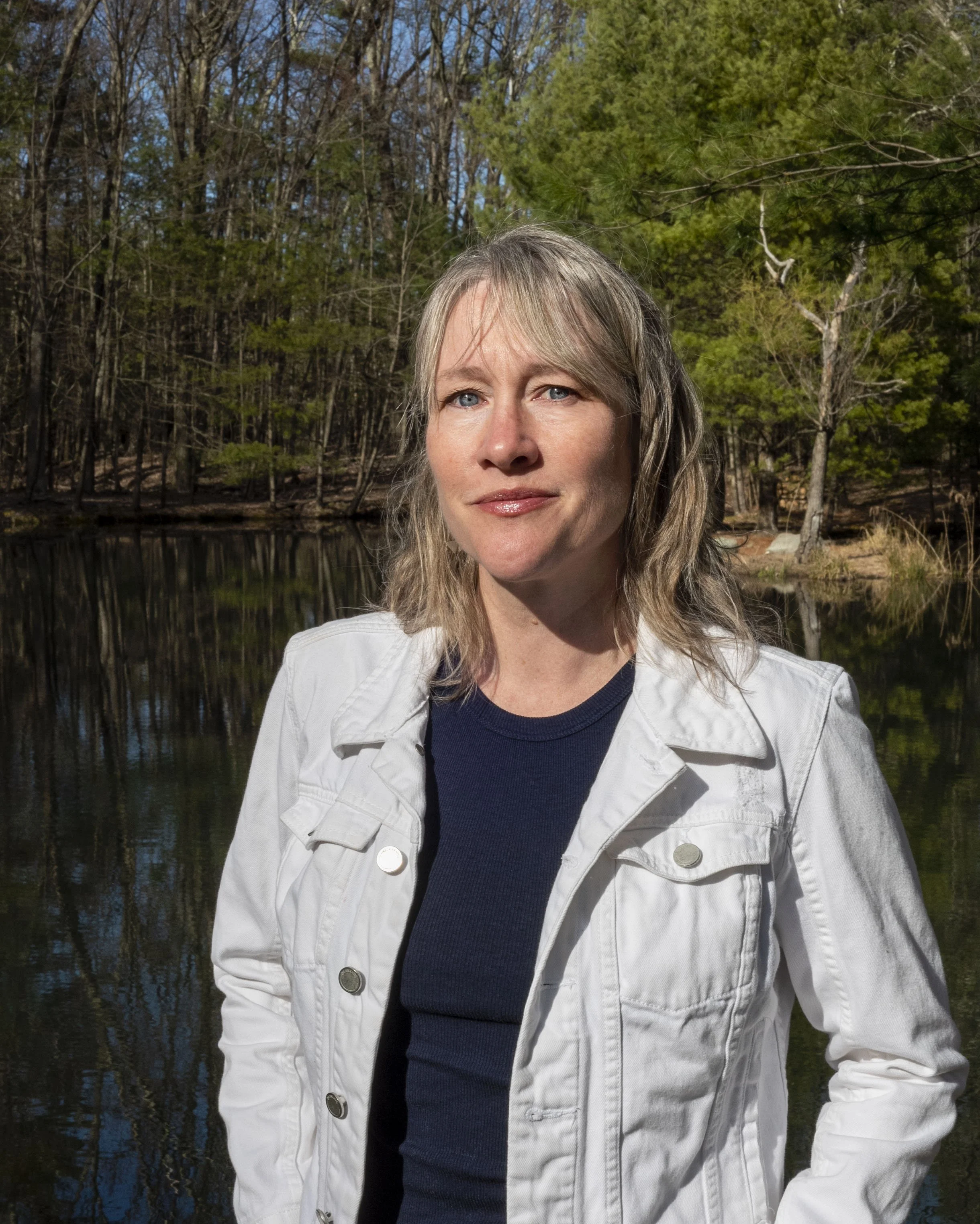 Woman in a white jacket standing by a forested lake