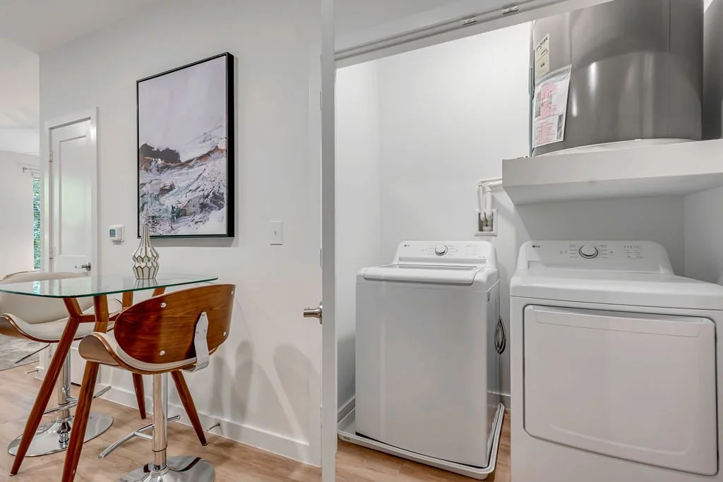A laundry room with a washing machine and dryer, and a dining area with a glass table and wooden chairs.