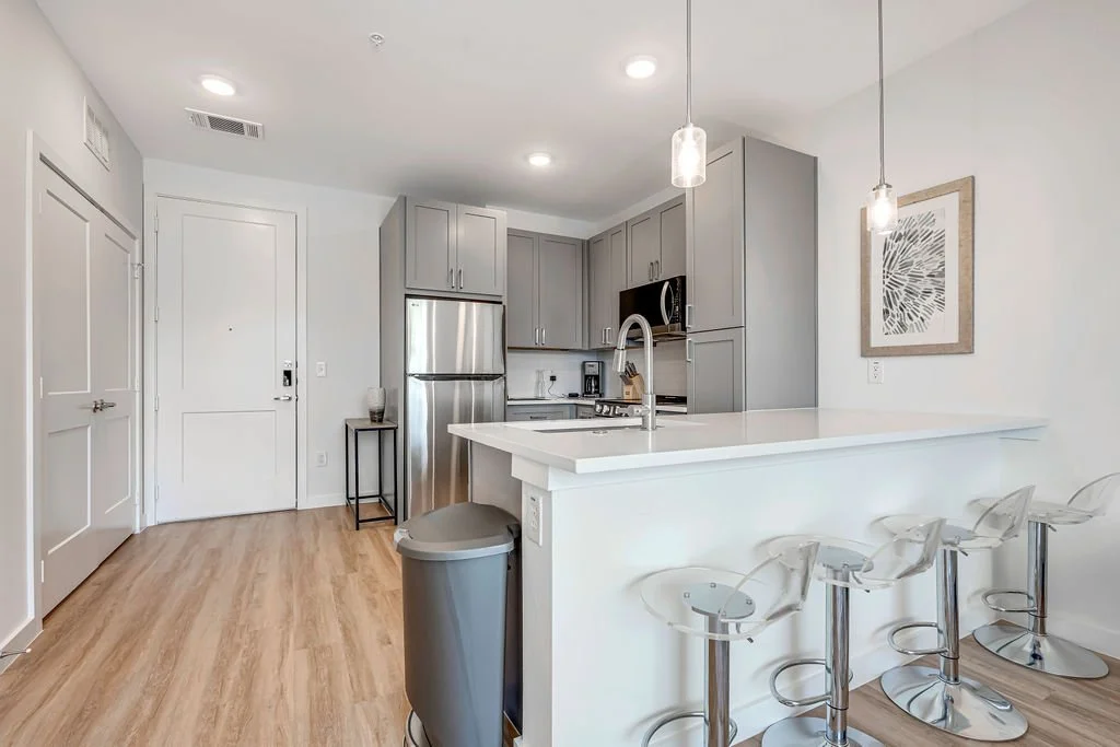 Modern kitchen with stainless steel appliances, gray cabinets, white countertop with bar stools, and wooden flooring.