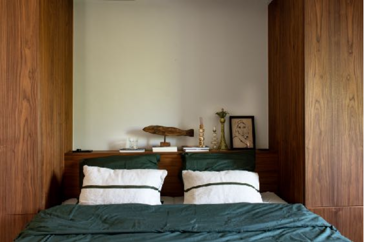 Een slaapkamer met een bed, witte kussens met zwarte strepen, een groene bedsprei, houten wandpanelen en decoratieve objecten op de hoofdbank.