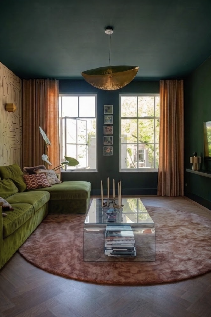 Een woonkamer met groene bank, een glazen salontafel, oranje gordijnen, een rotan plafondlamp, en een muur met houten panelen.