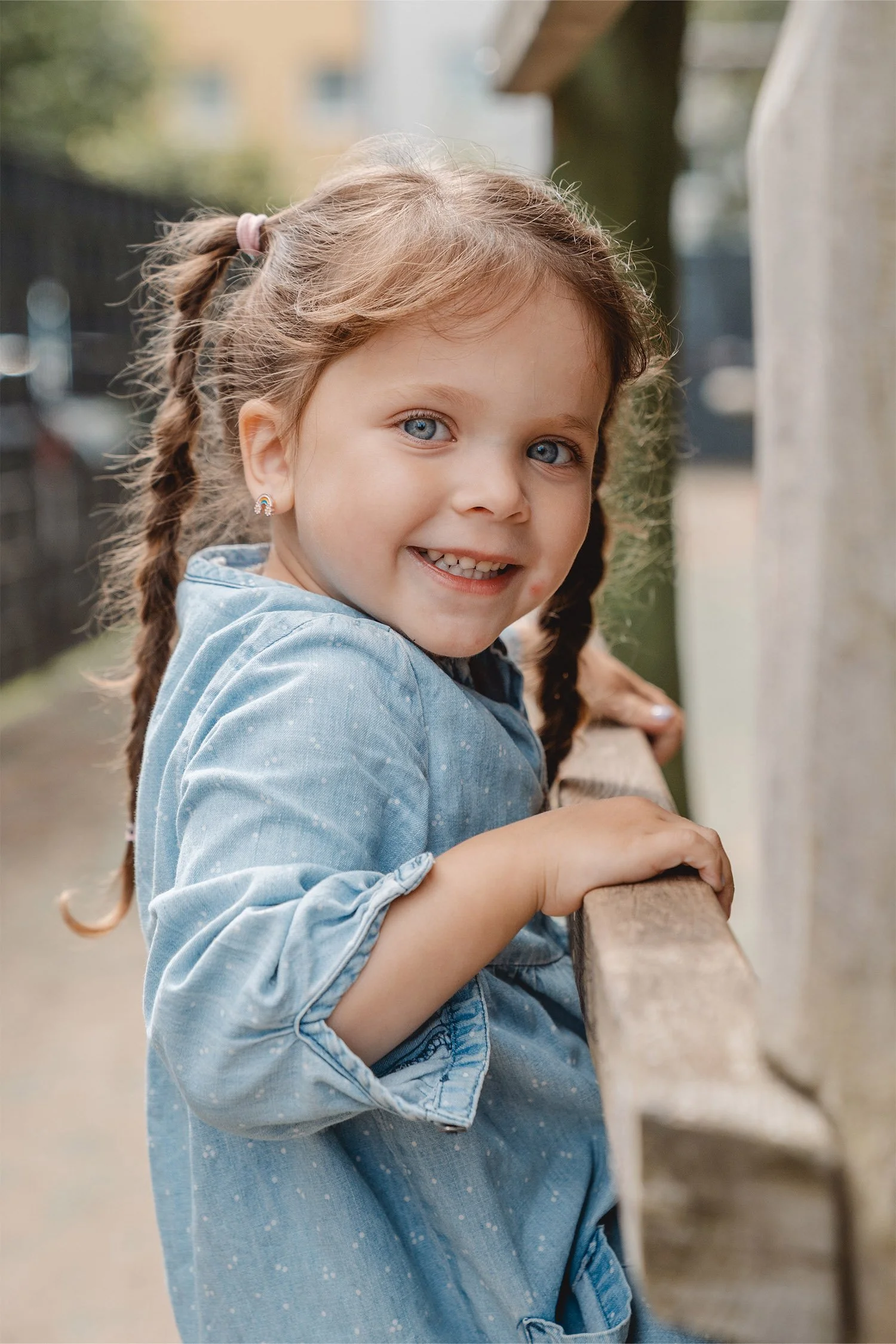Ein Portrait von einem Mädchen mit zwei braunen Zöpfen in einem blauen Kleid und strahlend blauen Augen. Sie klettert und hält sich am Klettergerüst fest. Dabei lächelt sie in die Kamera.