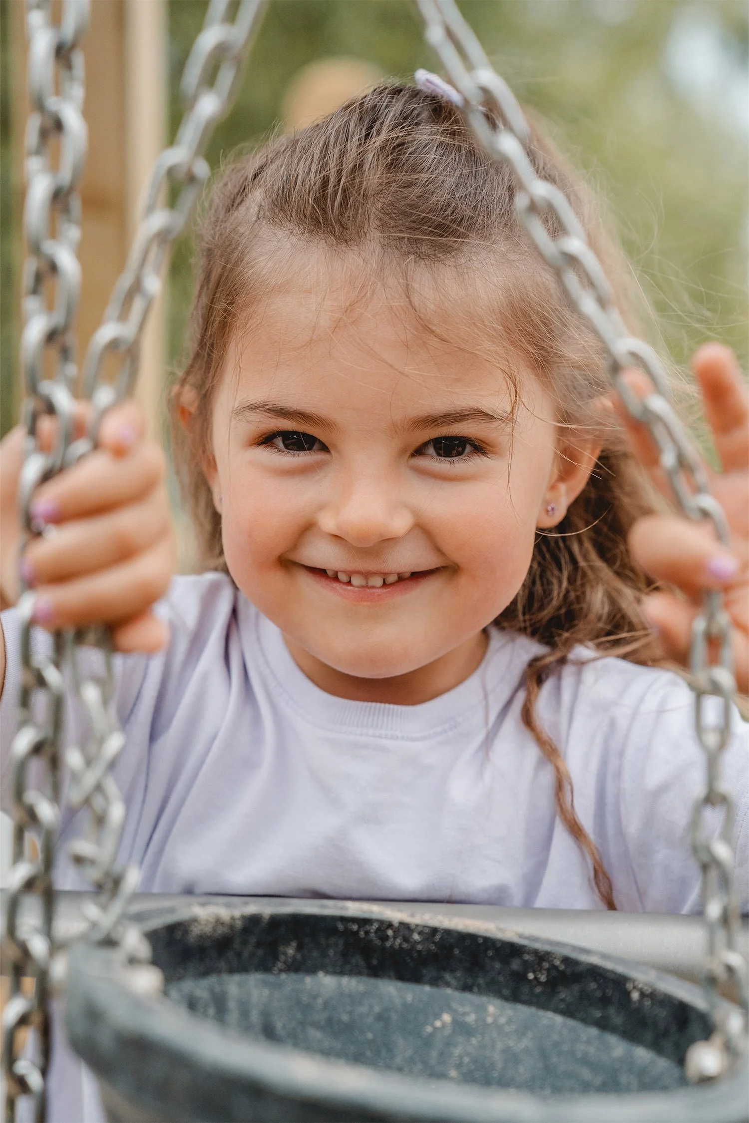 Ein Mädchen steht auf einem Klettergerüst und schiebt die Ketten an denen ein Eimer befestigt ist zu den Seiten, um zum Fotografen schauen zu können. Dabei lächelt Sie. 