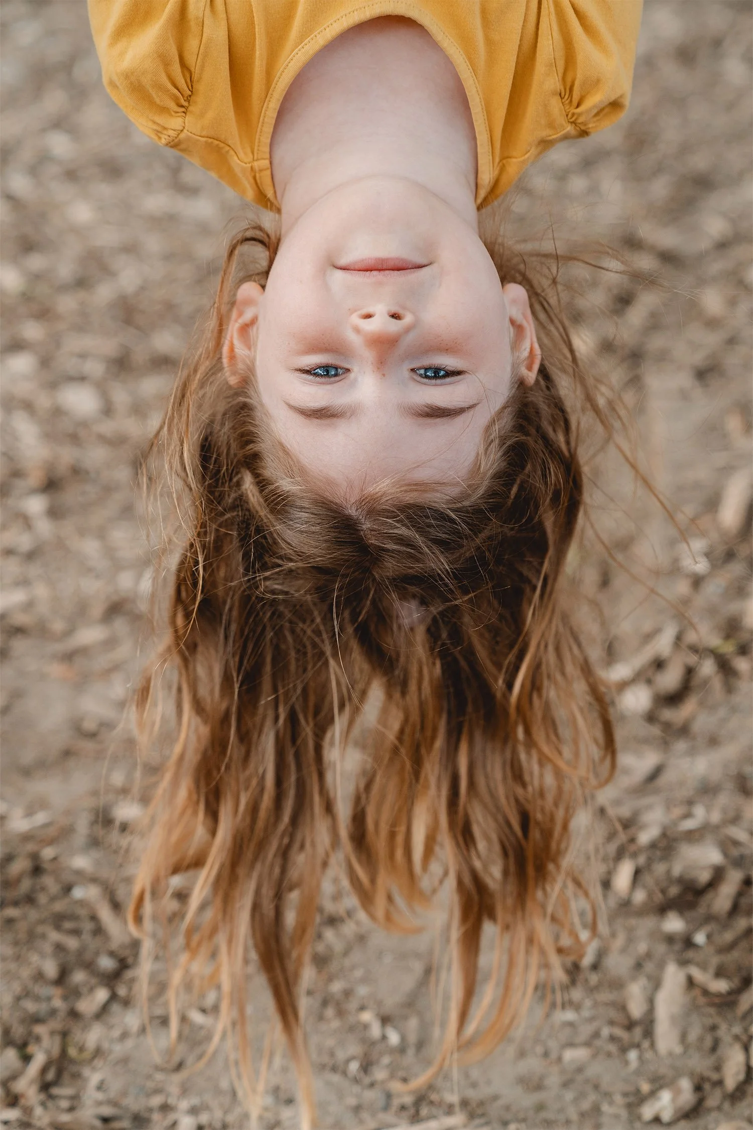 Kindergartenbild von einem brünetten Mädchen mit gelben T-Shirt. Sie hängt kopfüber und lächelt in die Kamera.