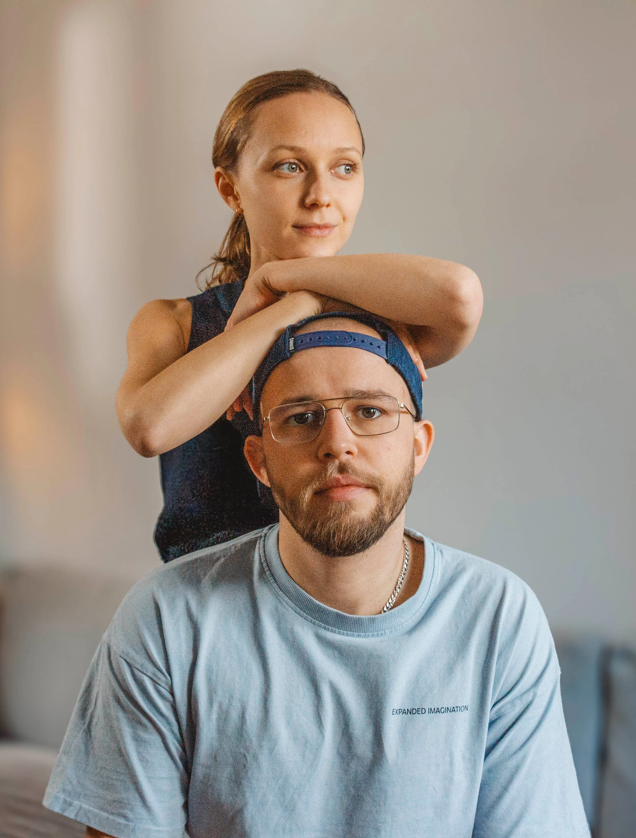 Portrait der Fotografen Julia und Pady: Pady sitzt und blickt direkt in die Kamera, während Julia hinter ihm steht, sich an seinen Kopf lehnt und lächelnd zur Seite schaut.